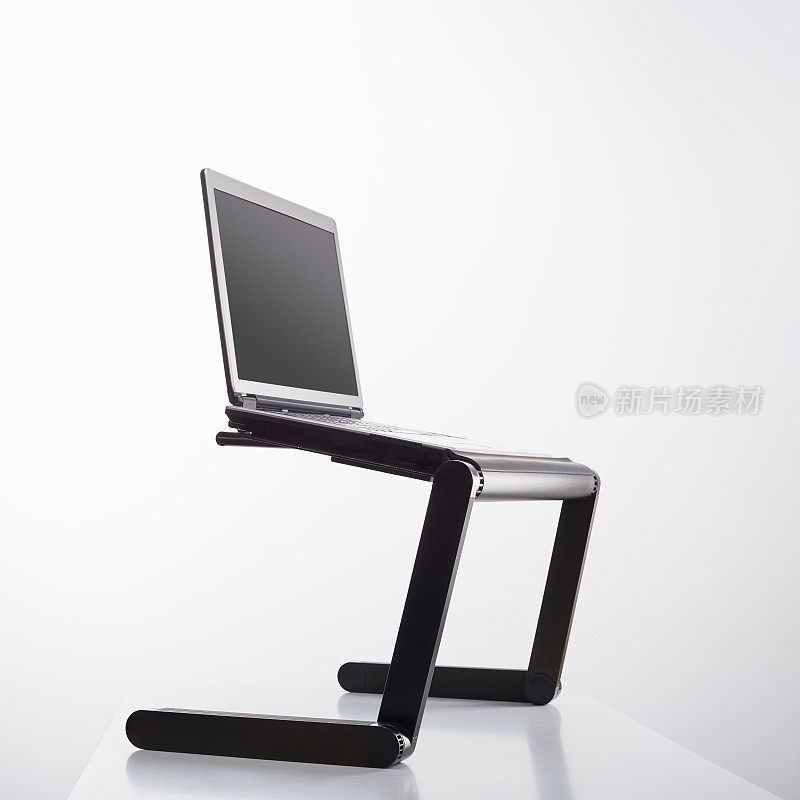 Laptop computer sits on a portable holder riser or stand against white background